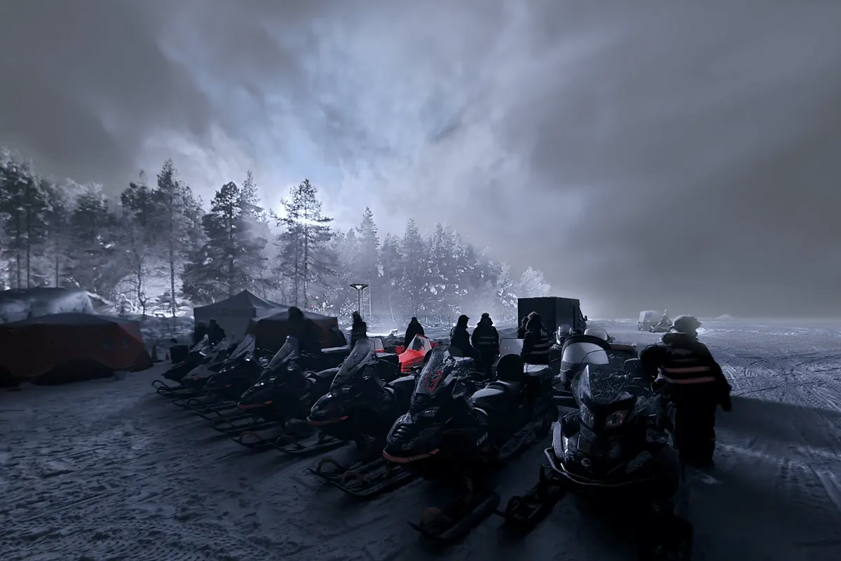 A line of snowmobiles and crew tents at a production basecamp in misty Arctic Finland