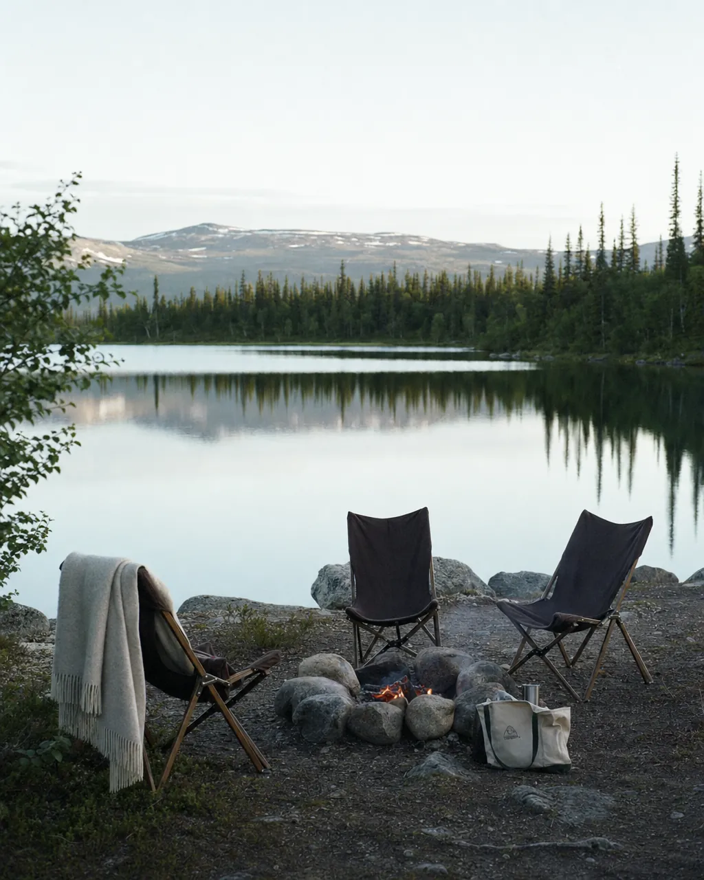 Five wooden canoes pulled up on a sand beach beside a mirror-still Lapland lake at midnight sun, distant pine-clad island