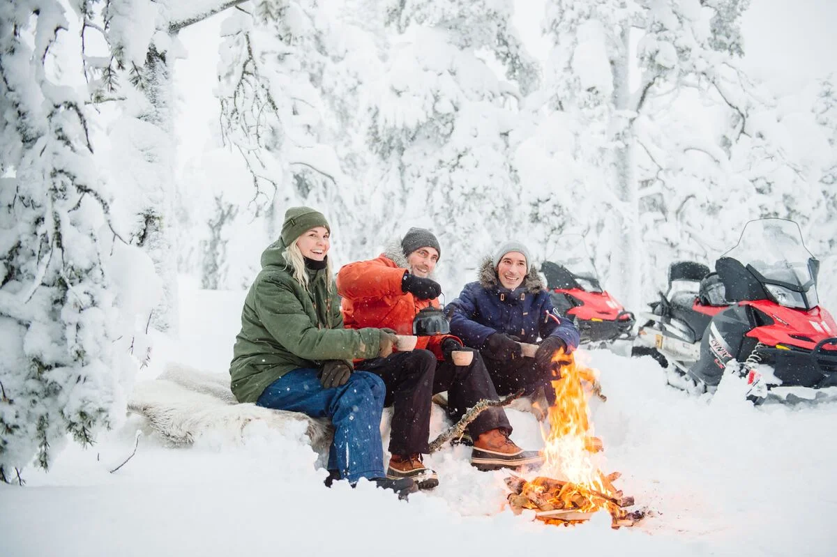 Snowmobile group warming up at a winter campfire in Pyhä-Luosto, Lapland — Nordic MICE producers and on-the-ground team operating across Finnish, Swedish, Norwegian and Icelandic Arctic