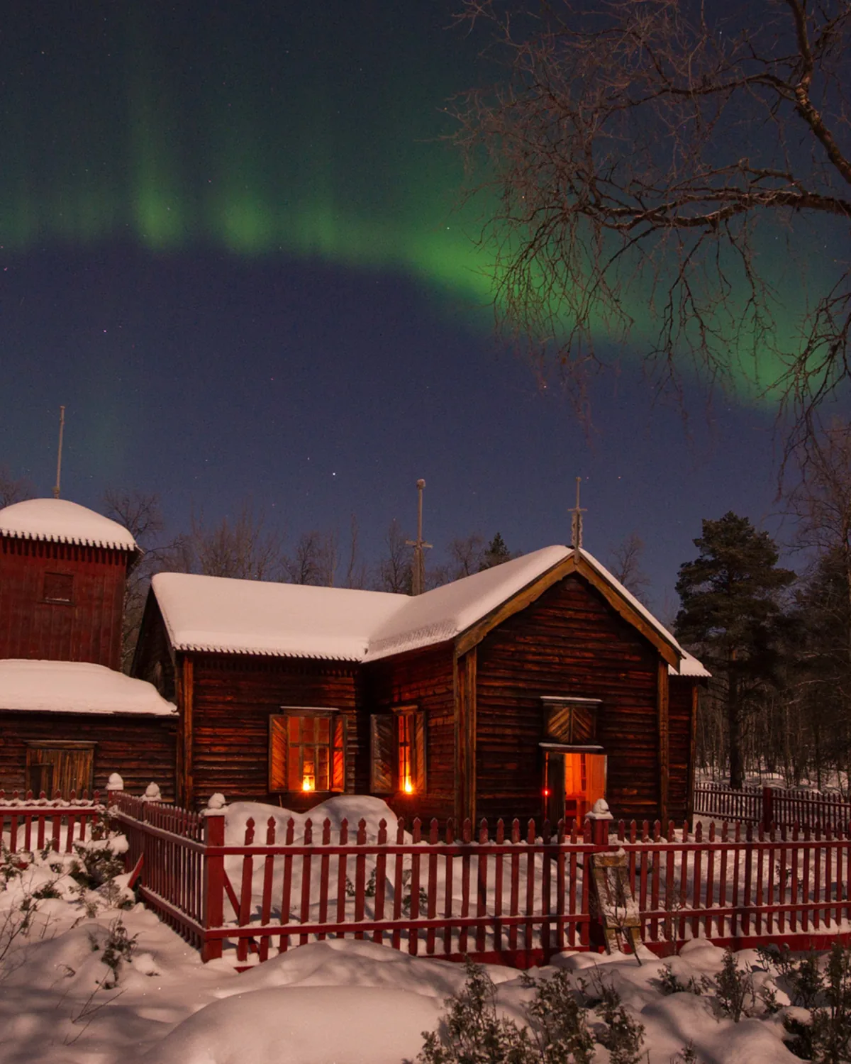 Pielpajärven erämaakirkko — Finland's only wilderness church near Inari, lit windows and a green aurora curtain over the snow-covered Sámi sanctuary